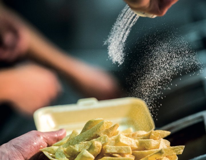 A hand pouring salt on a portion of chips