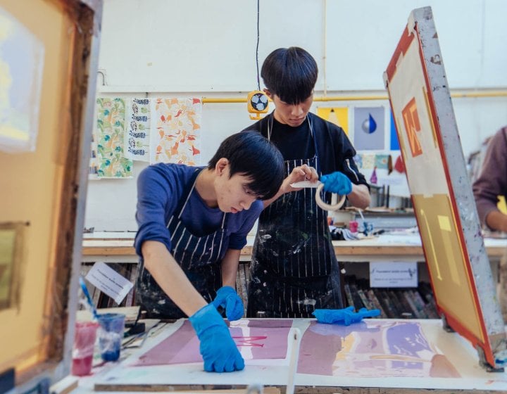 Two Falmouth University Graphic Design students screen printing in a studio