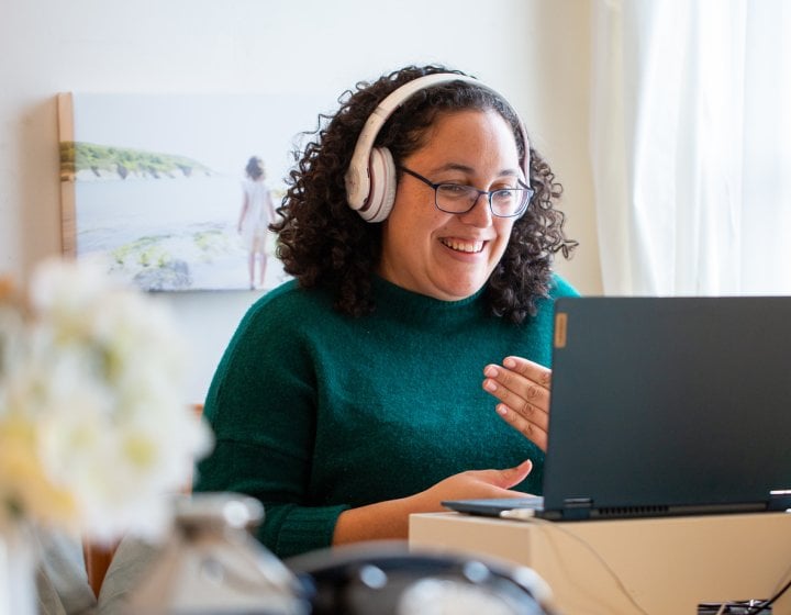 A woman wearing headphones smiling into her computer screen