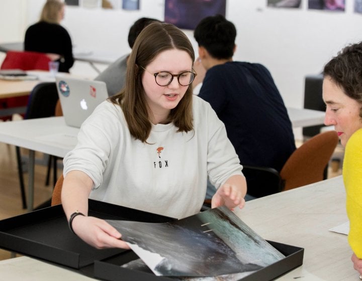 A female student showing a photograph from her portfolio to a female lecturer