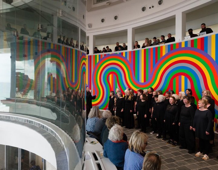 Line of people wearing black infront of rainbow background at Tate St Ives