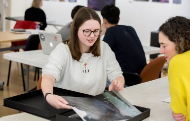 A female student showing a photograph from her portfolio to a female lecturer