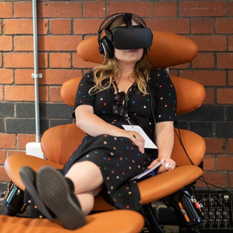 A woman sitting in an orange chair with VR headset on