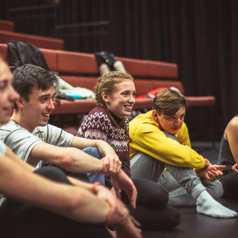 Group of students sat on theatre floor and smiling.