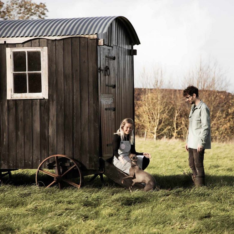 Falmouth alumni couple with a dog by a wooden trailer