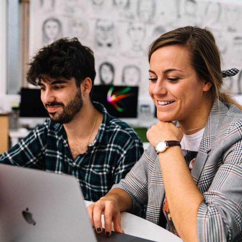 Two Falmouth University Creative Advertising students smiling at a laptop