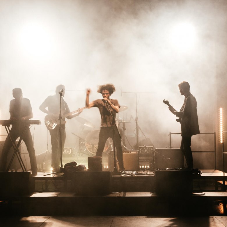 Shadowy figures of a four piece band playing on a smokey stage.