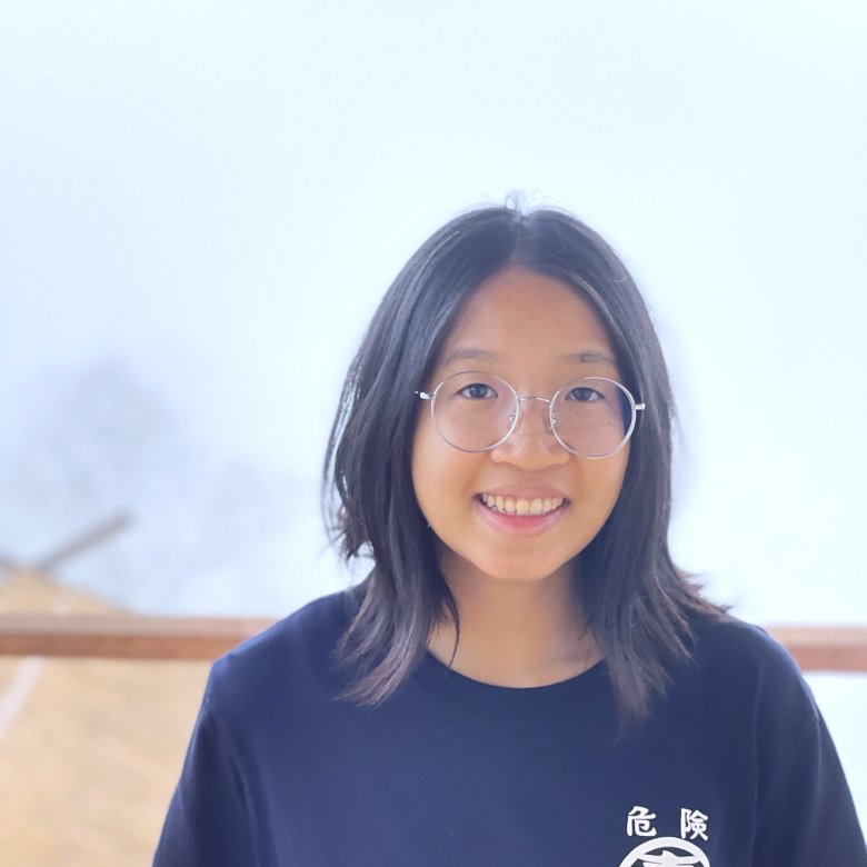 Photo of a student with shoulder length dark hair wearing round gold-framed glasses and a black t-shirt. 