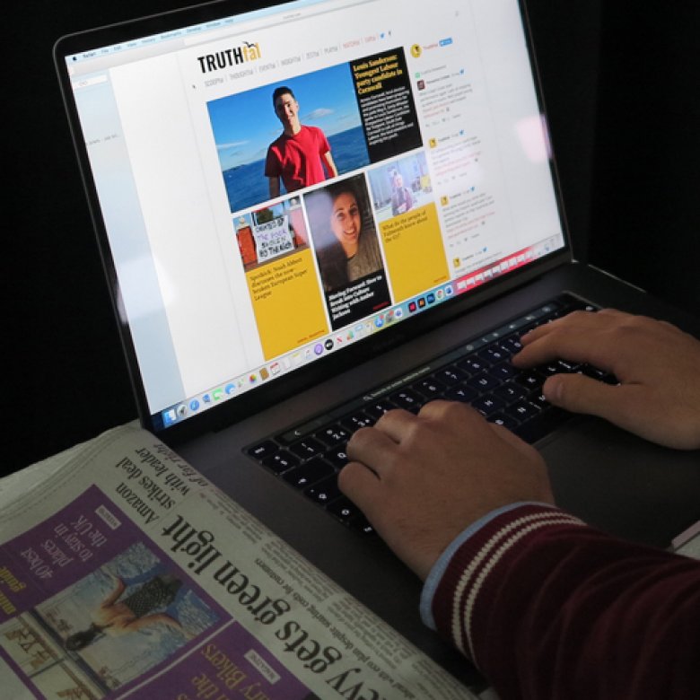 Hands typing on a laptop with a newspaper on a table