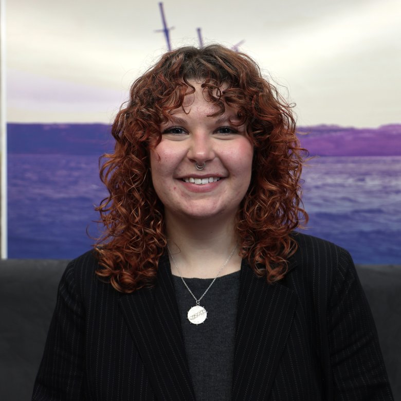 A woman smiling at the camera with a landscape picture in the background