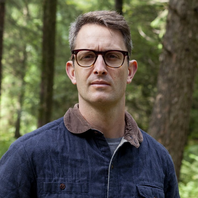 A man wearing glasses stood in a woodland 