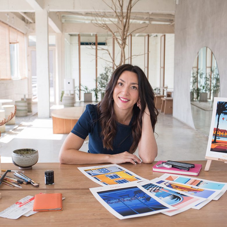 A head shot of illustrator Molly Maine, with long brown hair sitting at a wooden desk