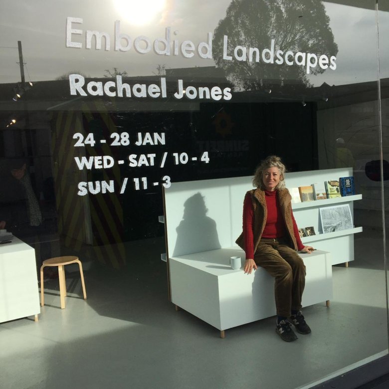 A woman sitting on a white sofa behind a large glass gallery window