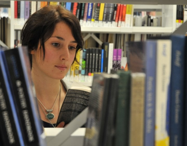 Student's face appearing through a gap in the books in the library.