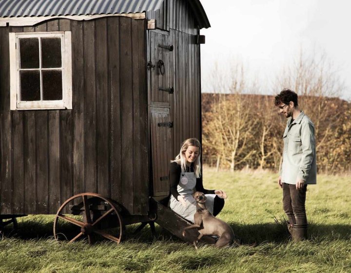 Falmouth alumni couple with a dog by a wooden trailer