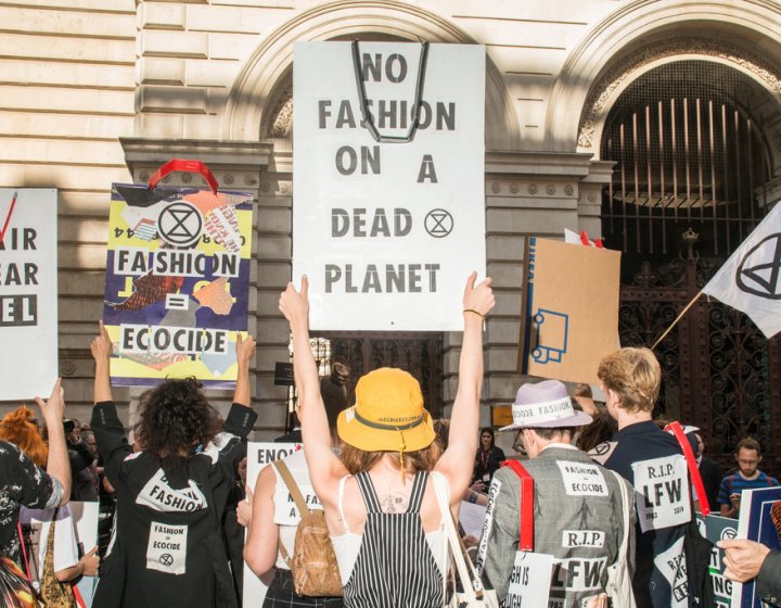 People gather to protest the fashion industry. A placard reads 'no fashion on a dead planet'