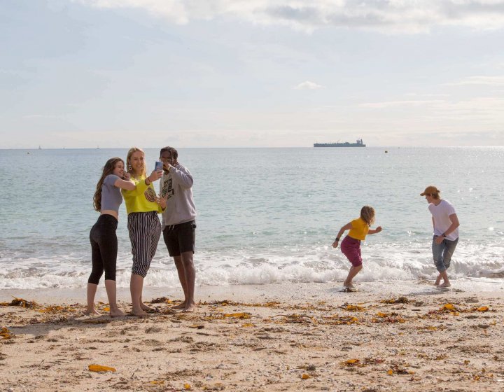 Five Falmouth University students on a sandy beach with the sea in the background