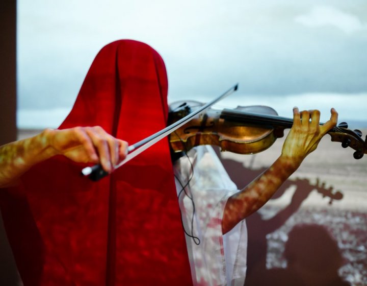 Person under a red shawl playing the violin