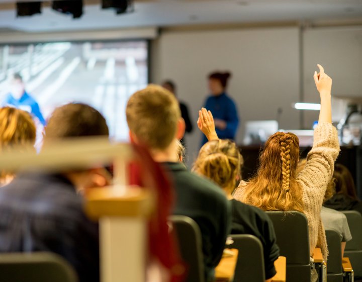 A lecture theatre with students raising their hands