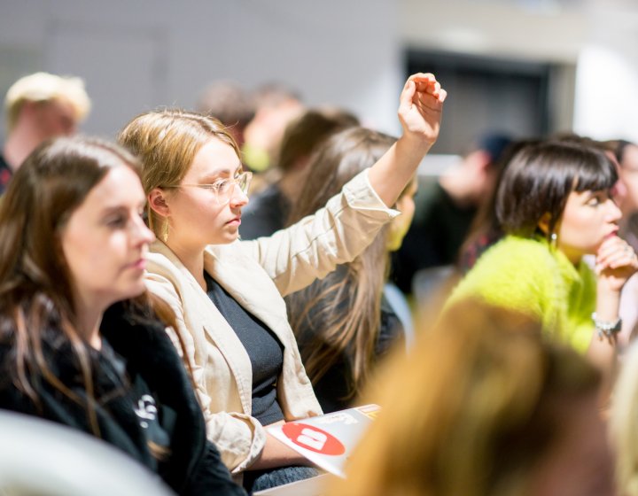 Female student raising hand in a crowd