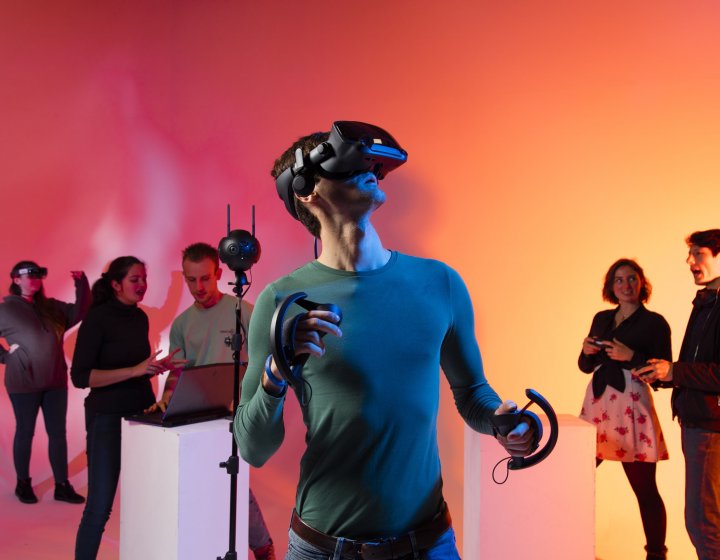 Games Academy students wearing a VR headset in front of an orange background