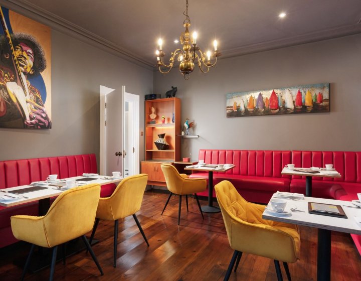 Dining space at Chelsea House in Falmouth. Red booth-style seating, gold chandelier, mustard velvet chairs, wooden flooring 