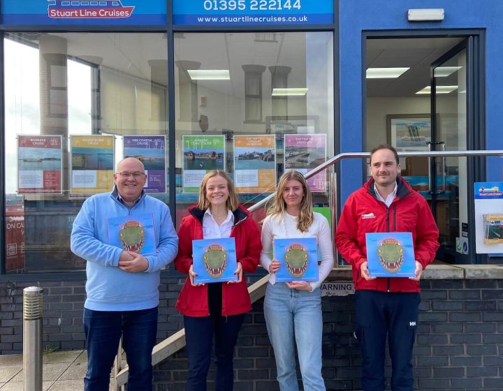 Four people standing outside Stuart Line Cruises shop front, holding a book with a dinosaur on the cover