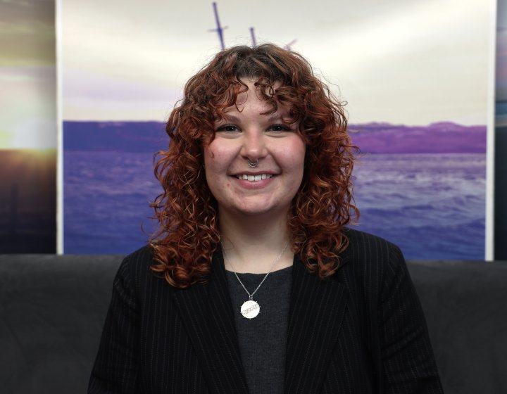 A woman smiling at the camera with a landscape picture in the background