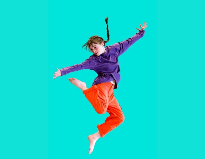 A young dancer jumping into the air set against a mint green background