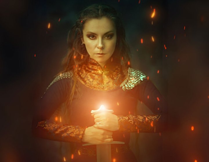 A celtic women looking at the camera holding a glowing sword