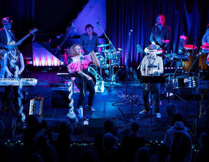 A large band ensemble on stage performing under theatrical lighting that is bring and colourful