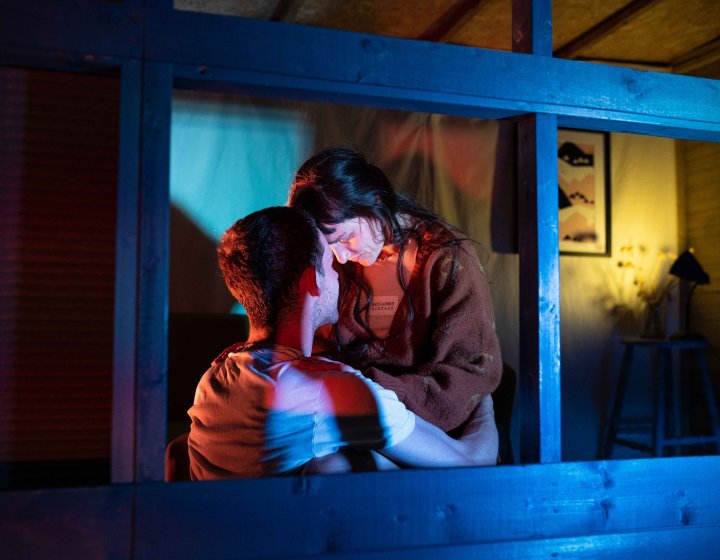 Two performers in close proximity to each other within a shed structure with blue and cold lighting colours on them