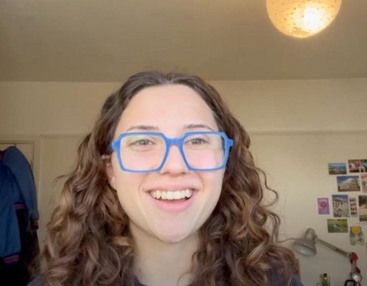 A young woman smiling, wearing blue glasses