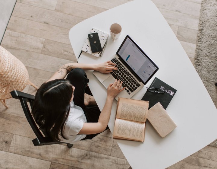 A birds eye view shot of a woman sitting at a desk with laptop and notepad