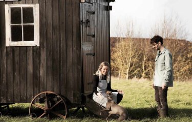 Falmouth alumni couple with a dog by a wooden trailer