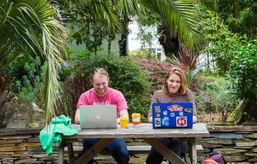 Students working at laptops below palm tree on Falmouth campus.