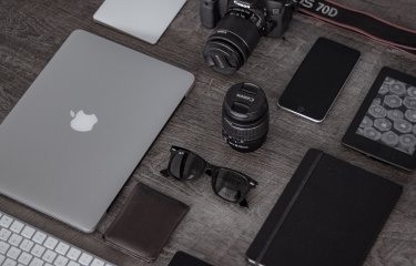 A desk with laptop, keyboard, camera, lens, smartphone.