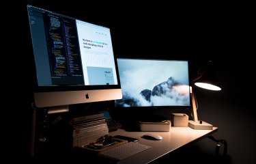 Desktop screens lit up in a dark room.