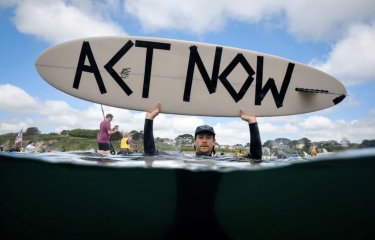 Activist in the sea holding up a surfboard with Act Now message written on it