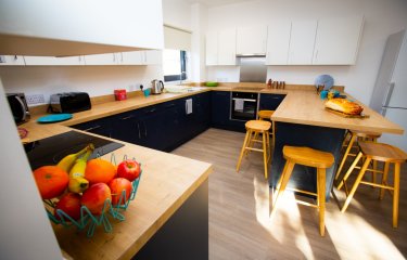 A student kitchen equipped with toaster, kettle, microwave, table, chairs and an oven