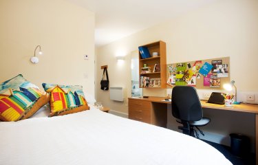 An empty university room, equipped with double bed and desk