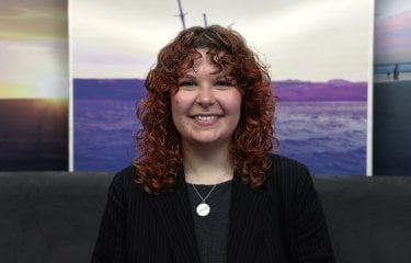 A woman smiling at the camera with a landscape picture in the background