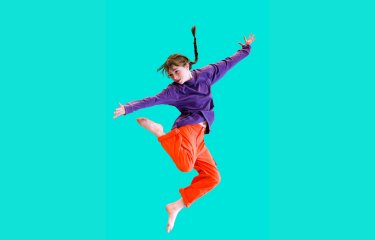 A young dancer jumping into the air set against a mint green background