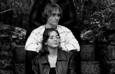 A black and white image of three people sat in a line on some external stone steps