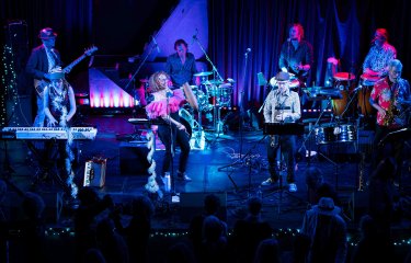 A large band ensemble on stage performing under theatrical lighting that is bring and colourful