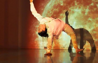 A performer on stage in a dance position with the projection of the sun behind them
