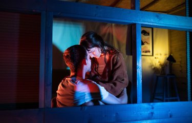 Two performers in close proximity to each other within a shed structure with blue and cold lighting colours on them