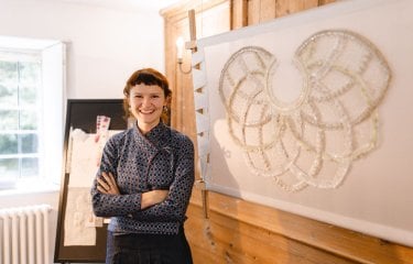 A woman stood by a large piece of embroidery