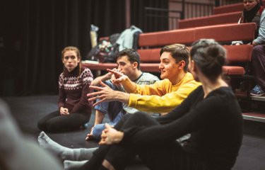 Group of students sat in performance space discussing acting
