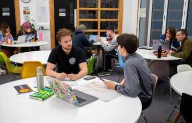 Two male Creative advertising students engaged in conversation at a table